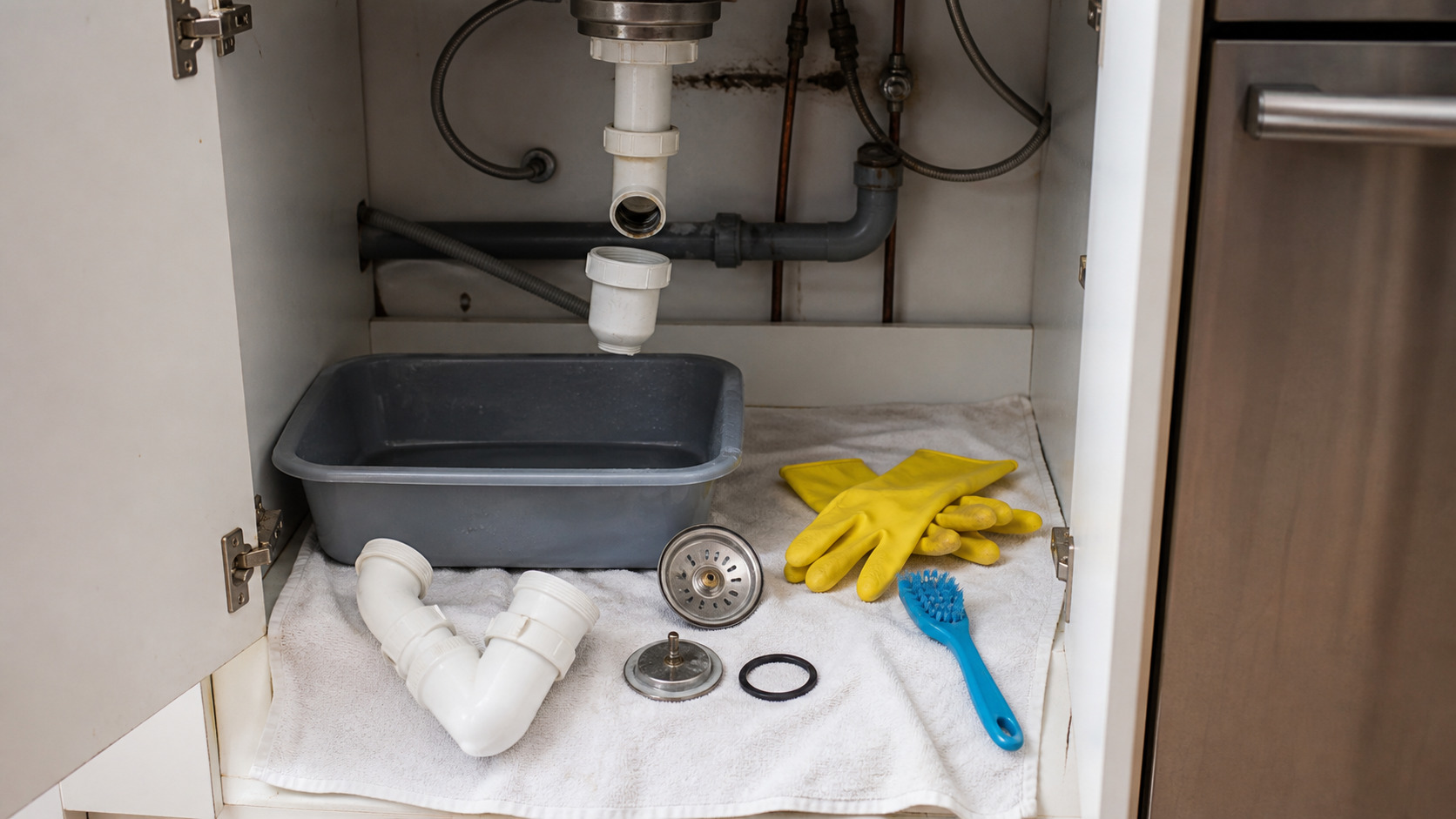 Siphon d'évier démonté avec gants, bassine et bonde nettoyée
